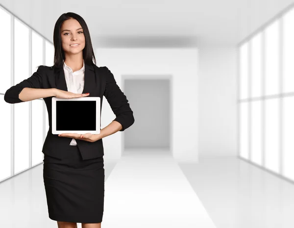 Office girl standing on background of light interior and showing screen tablet