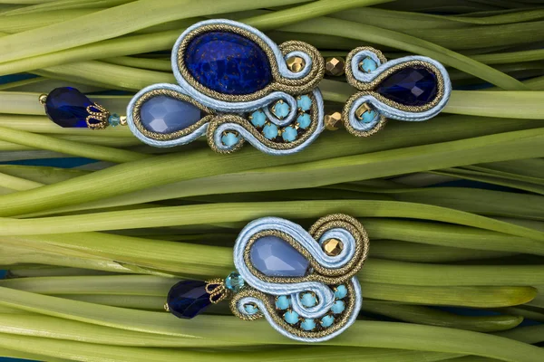 Soutache bijouterie blue earrings with blue stones and light-blue and cyan crystals on the green background of grass stems