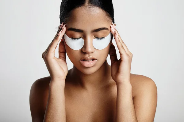 Woman with eyes patches touching temples