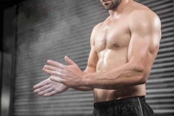 Mid section of shirtless man clapping hands with talc