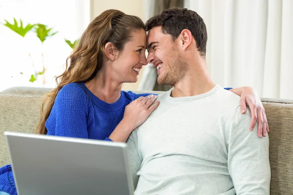 Young couple smiling face to face on sofa and using laptop