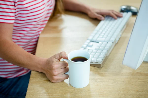 Female hands holding a coffee cup and typing