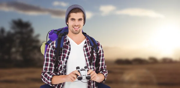 Happy hipster wearing backpack holding binoculars