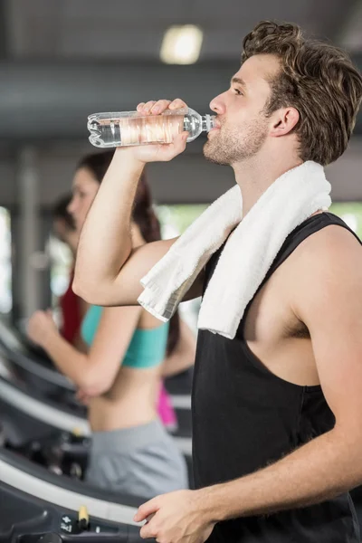 Athletic man drinking water while running on treadmill