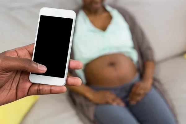 Man using phone and pregnant woman relaxing on sofa