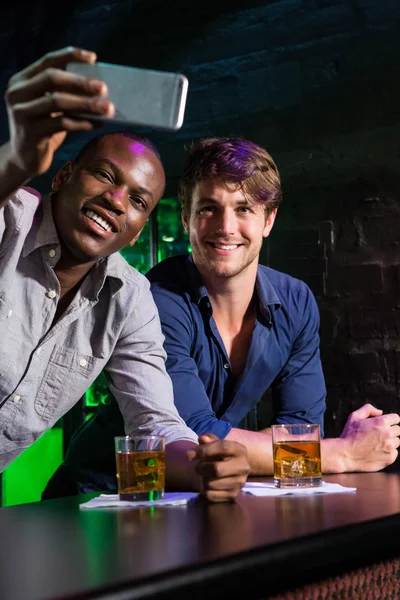 Two men taking a selfie on phone at bar counter