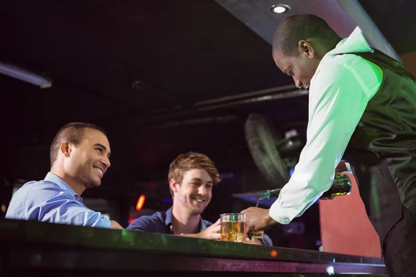 Bartender serving whiskey to two men at bar counter