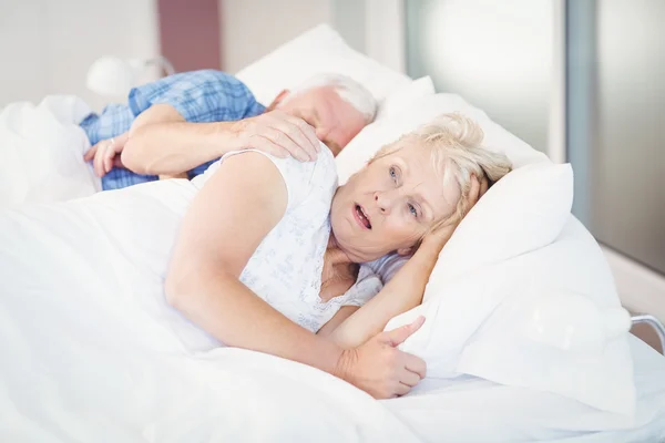 Shocked senior woman sleeping besides man on bed