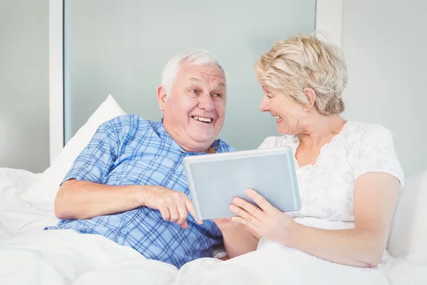 Cheerful senior couple using digital table on bed