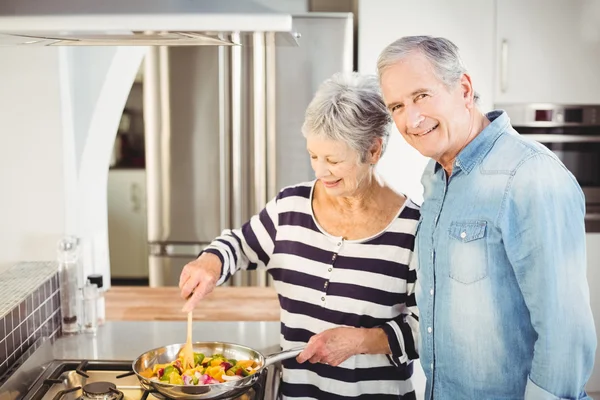 Senior man standing with wife cooking food