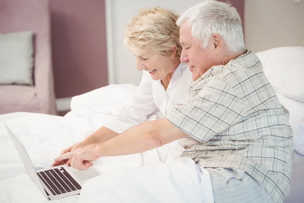 Smiling senior couple laughing while using laptop