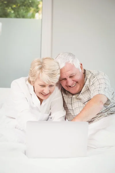 Happy couple laughing while using laptop in bed