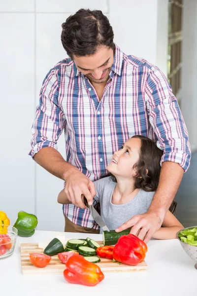 Father teaching daughter to cut vegetable