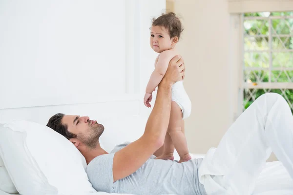 Father playing with crying daughter on bed