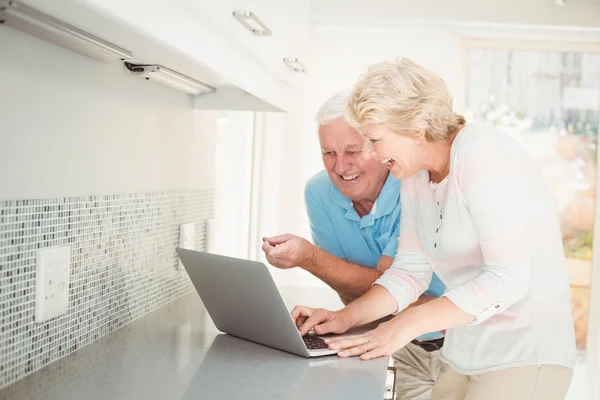 Senior couple laughing while using laptop in kitchen