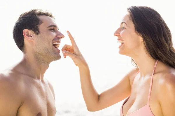 Happy woman applying moisturizer on mans nose