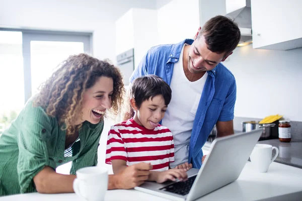 Parents using laptop with son in kitchen