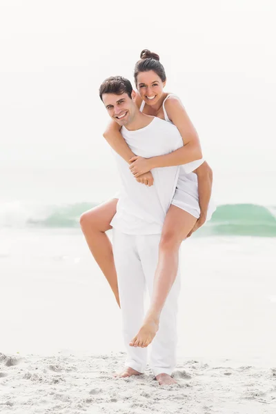 Man giving a piggy back to woman on the beach