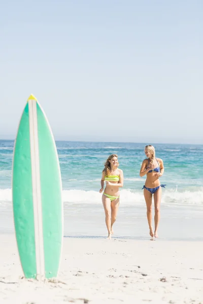 Surfboard in sand and two women running