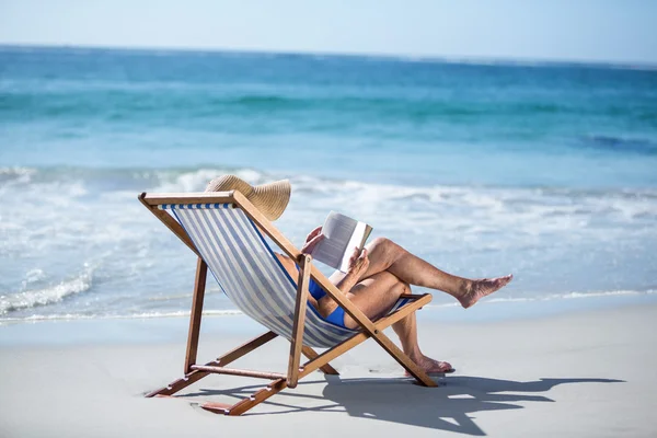 Pretty mature woman reading a book lying on deck chair