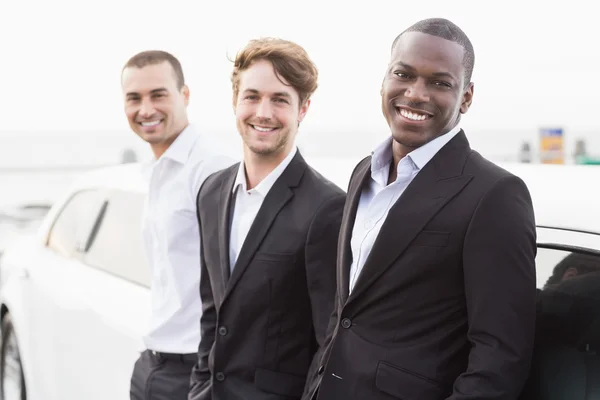 Well dressed men posing leaning on a limousine