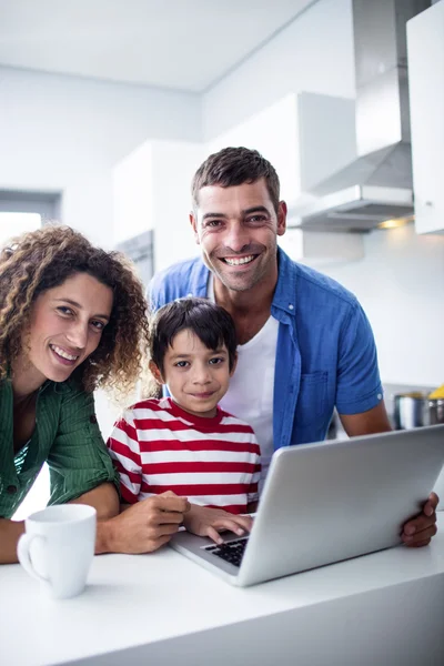 Parents using laptop with son in kitchen