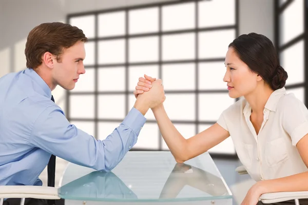 Business couple arm wrestling at desk