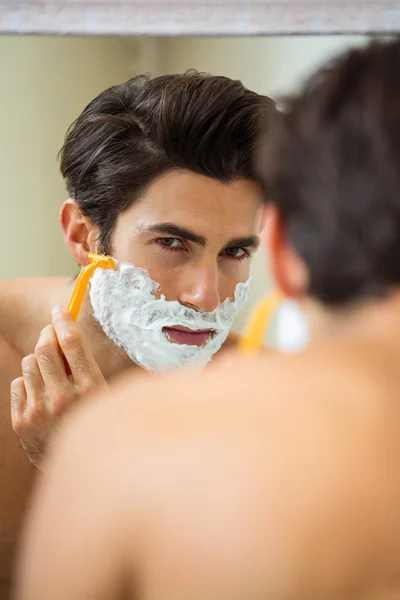 Man reflecting in mirror while shaving beard