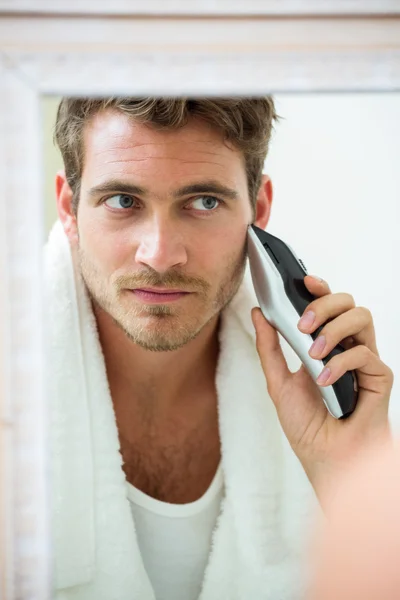 Man in mirror shaving with trimmer