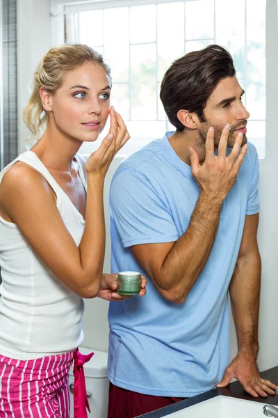Man and woman applying moisturizer on face