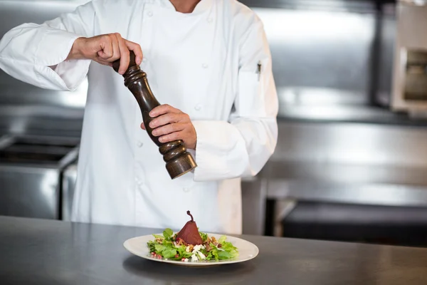 Chef grinding pepper on salad