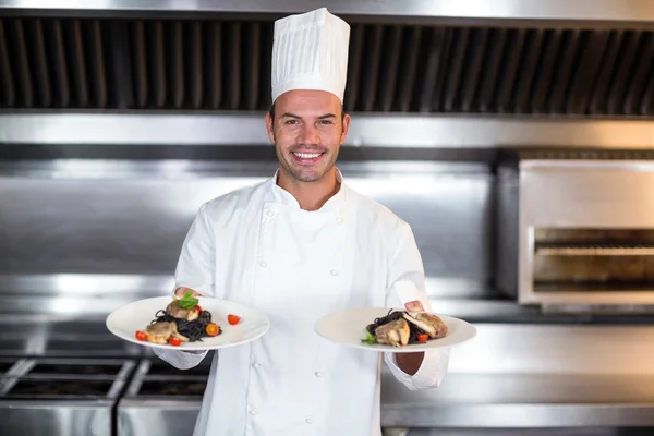 Portrait of smiling chef holding plates in kitchen