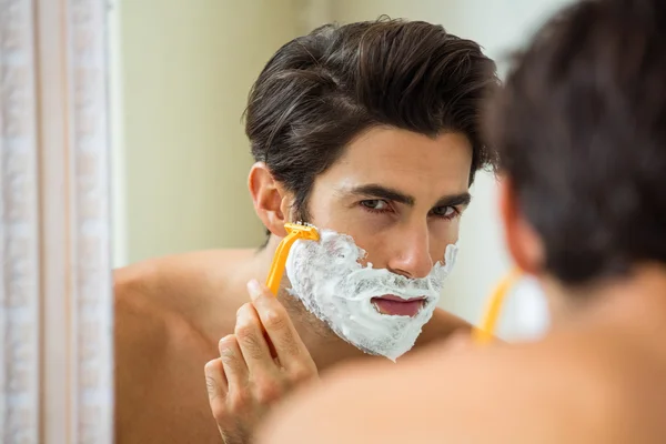 Man reflecting in mirror while shaving beard