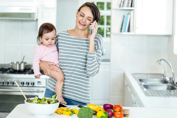 Woman carrying daughter while talking on cellphone