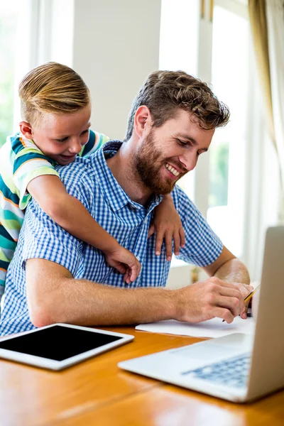 Smiling son leaning on father working at home