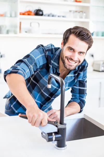Man fixing tap with tool in kitchen