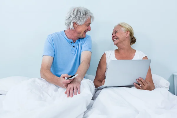 Couple using laptop while sitting on bed