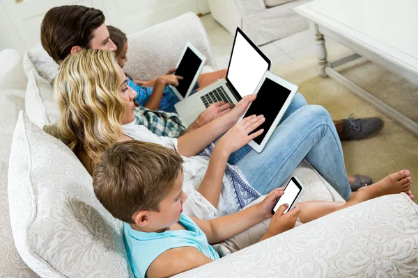Family using various technologies on sofa