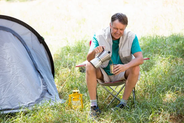 Senior man is crouching beside his tent