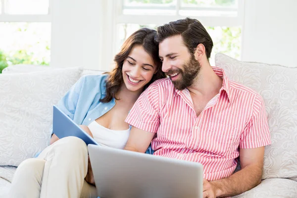 Couple using digital tablet and laptop in living room