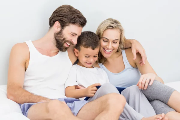 Parents and son sitting on bed and using digital tablet