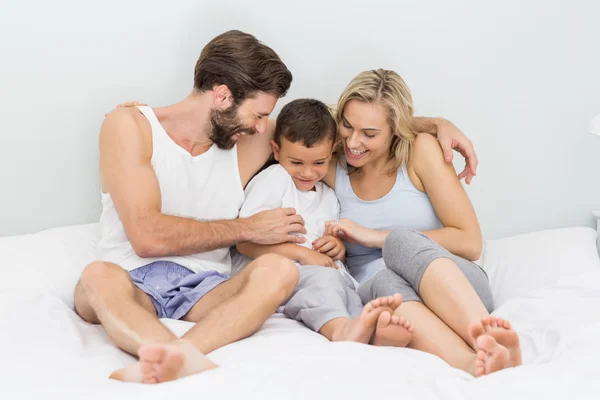 Parents and son sitting on bed and having fun
