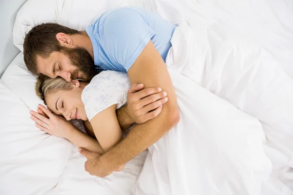 Man embracing woman while sleeping on bed