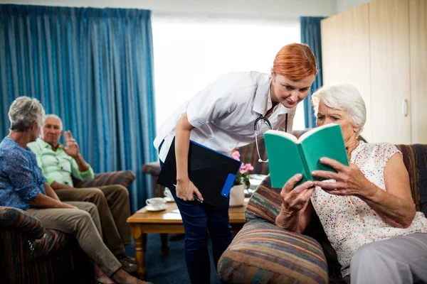 Senior woman reading book with nurse