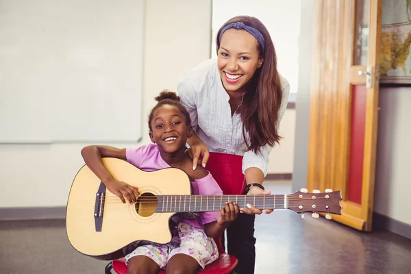 Teacher assisting a girl to play a guitar