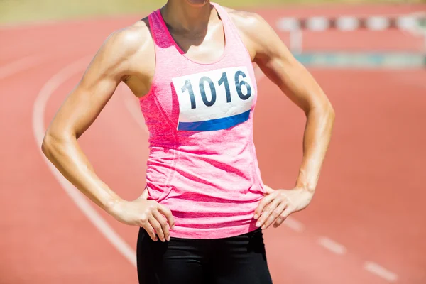 Mid section of female athlete standing with hands on hips