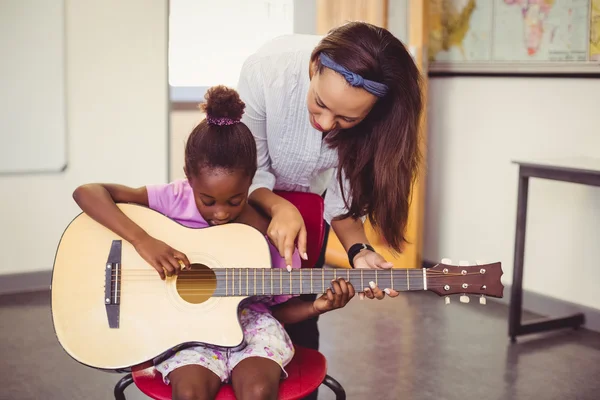 Teacher assisting a girl to play guitar