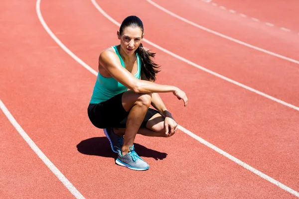 Portrait of female athlete kneeling on running track