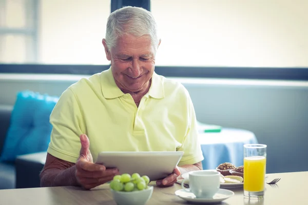 Senior man using digital tablet while having breakfast