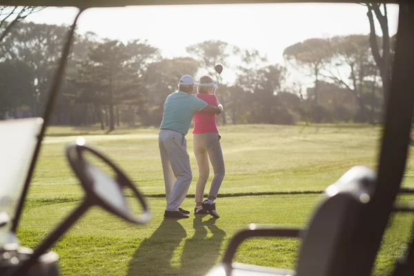 Mature man teaching woman to play golf
